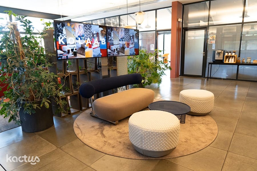 Espace d’accueil moderne chez Kolaab avec canapés design, écrans muraux et plantes vertes.