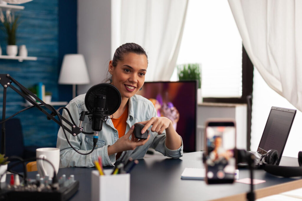Une créatrice de contenu souriante enregistrant une vidéo pour TikTok, assise à son bureau avec un micro et un équipement de podcast, illustrant la création de contenu marketing sur les réseaux sociaux.