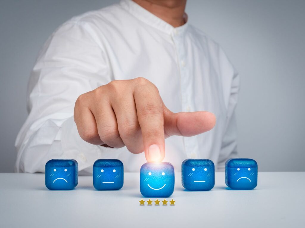 Un homme pointe sur un cube lumineux souriant affichant cinq étoiles de satisfaction client, parmi des cubes exprimant diverses émotions.