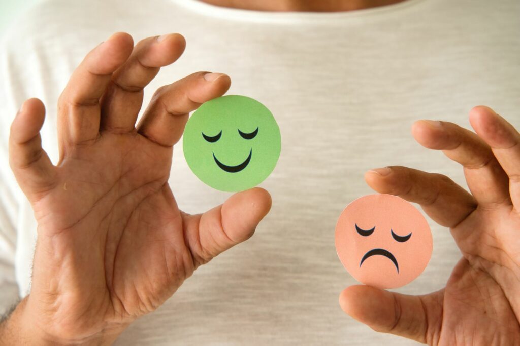 Un homme tenant deux émoticônes, l'une souriante et l'autre triste, symbolisant les réponses d'un questionnaire de satisfaction