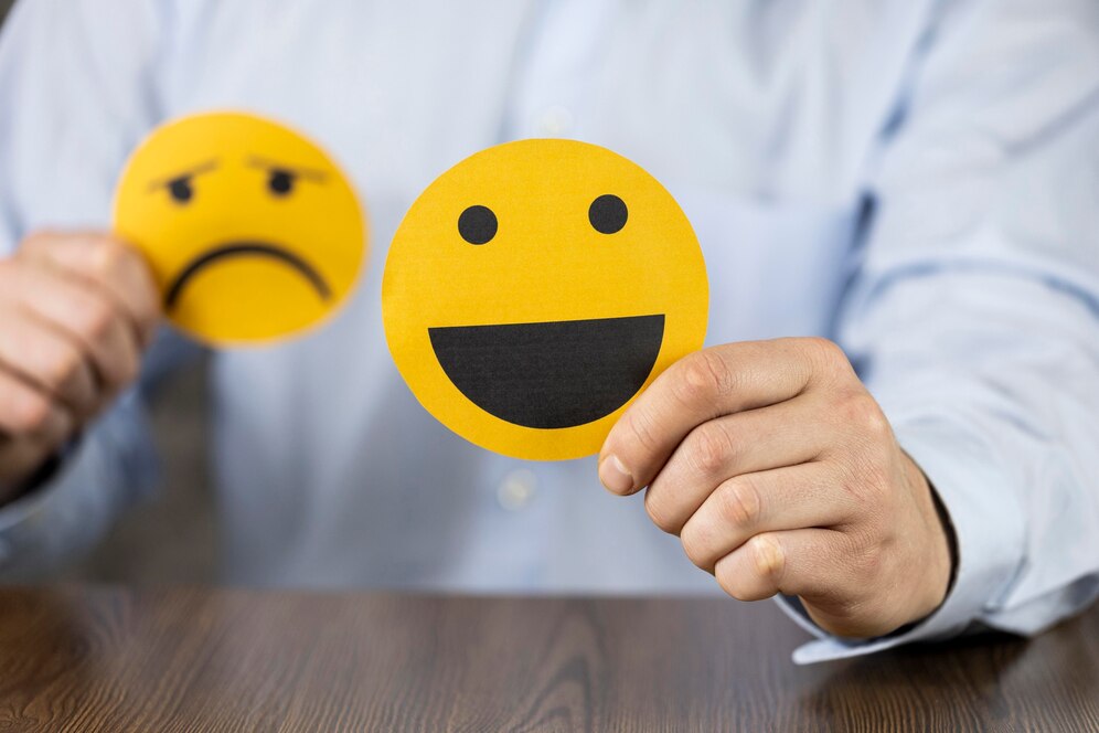Un homme en chemise tient deux émoticônes contrastés : un sourire heureux et une mine triste, illustrant les deux facettes de la satisfaction client dans la relation client.