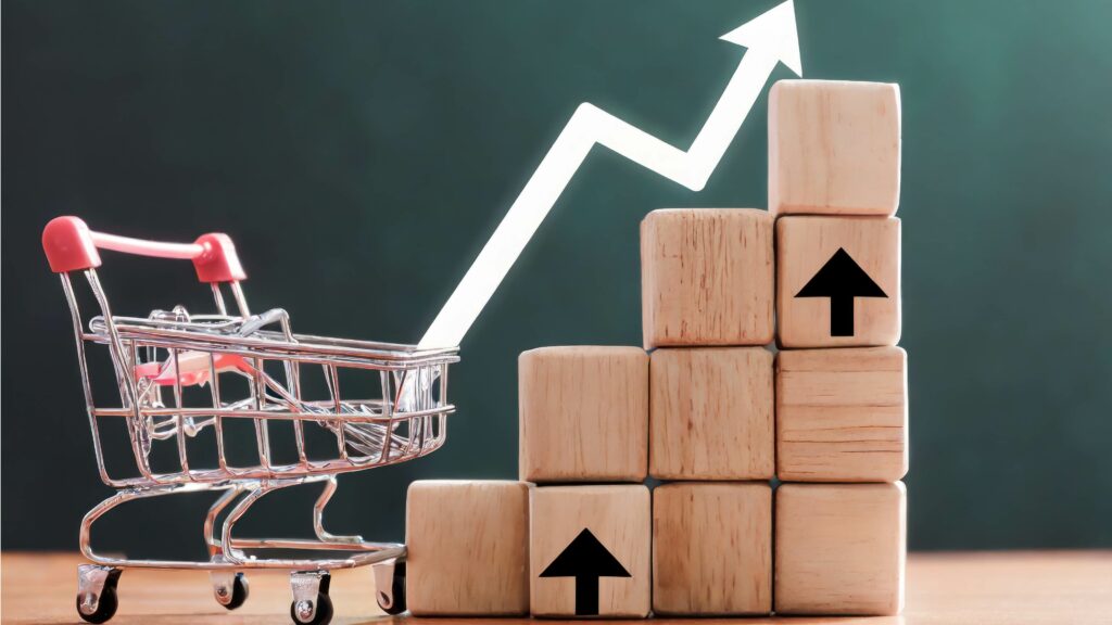 Un chariot miniature est posé à côté d'une pile de blocs en bois avec des flèches noires pointant vers le haut. Une flèche blanche pointant vers le haut superposée sur l'image symbolise la croissance des affaires ou l'augmentation des ventes. L'arrière-plan est un dégradé de vert et de vert foncé.