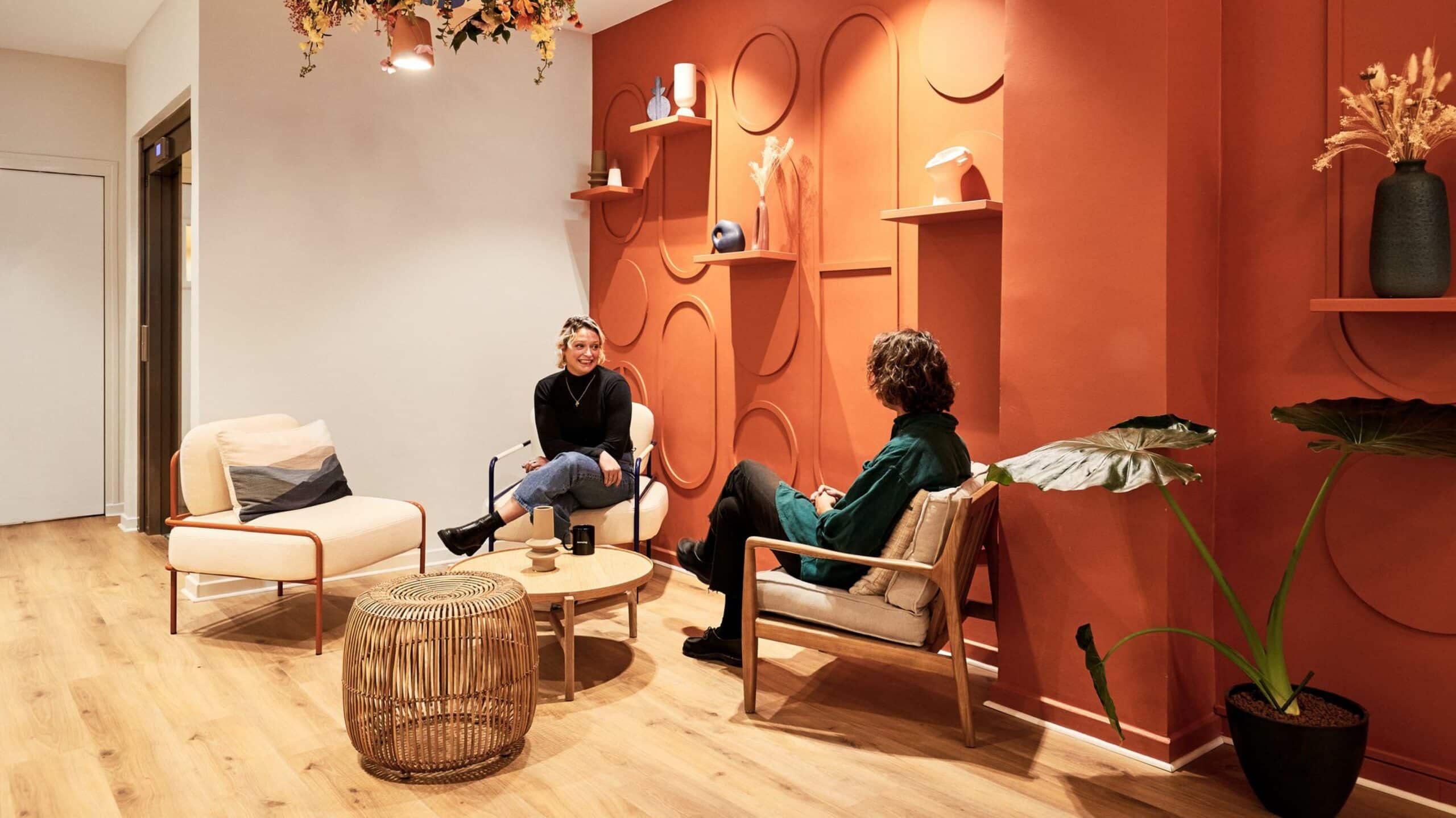 Salle de réunion lumineuse et moderne avec des tables en bois clair, des chaises assorties, et des plantes d'intérieur. Les murs blancs sont décorés de grands miroirs circulaires, ajoutant une touche design à l'espace. Le sol en bois et les tapis doux complètent l'ambiance chaleureuse et accueillante.