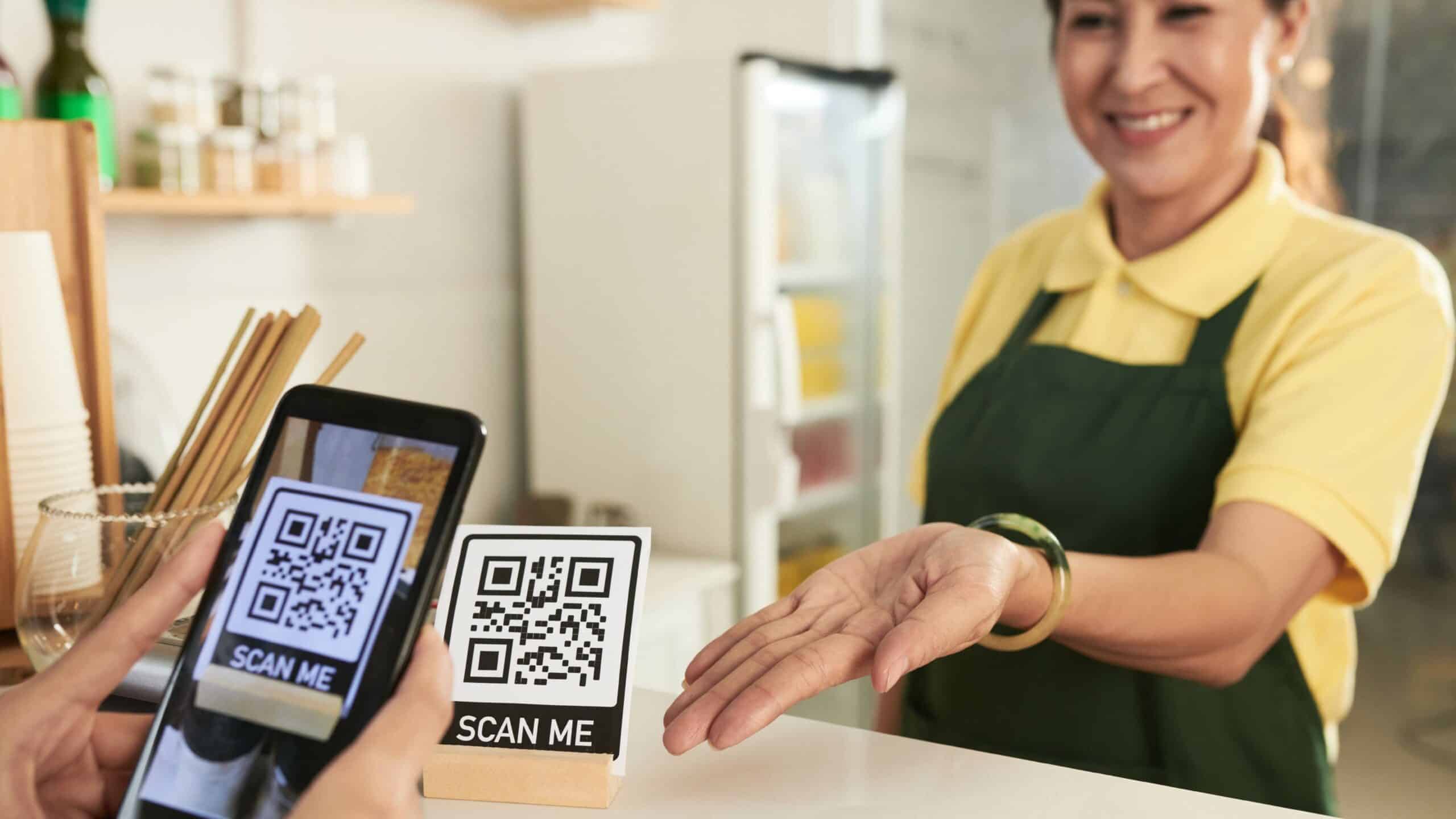 Client scannant un QR code en caisse avec son smartphone pendant que l'employée sourit.